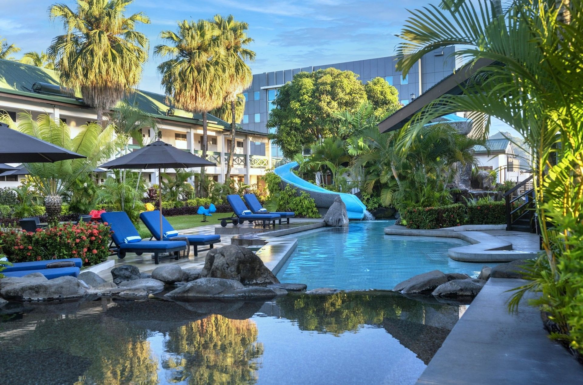 Bright blue loungers under a black patio umbrella by a winding swimming pool at TokaToka Resort Nadi Fiji