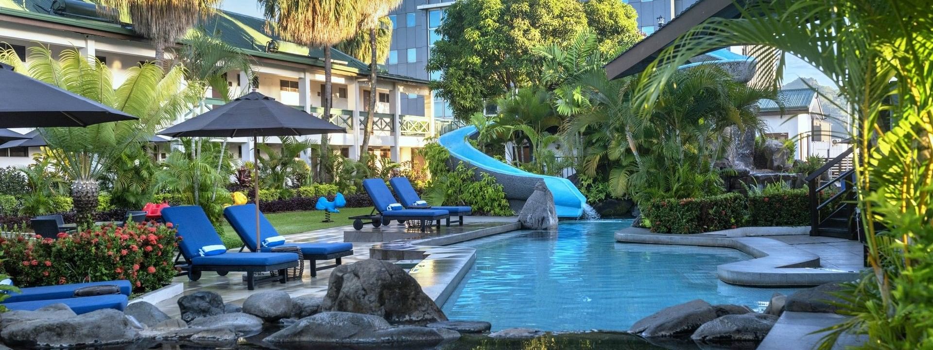 Bright blue loungers under a black patio umbrella by a winding swimming pool at TokaToka Resort Nadi Fiji
