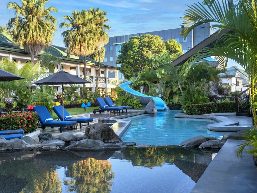 Bright blue loungers under a black patio umbrella by a winding swimming pool at TokaToka Resort Nadi Fiji