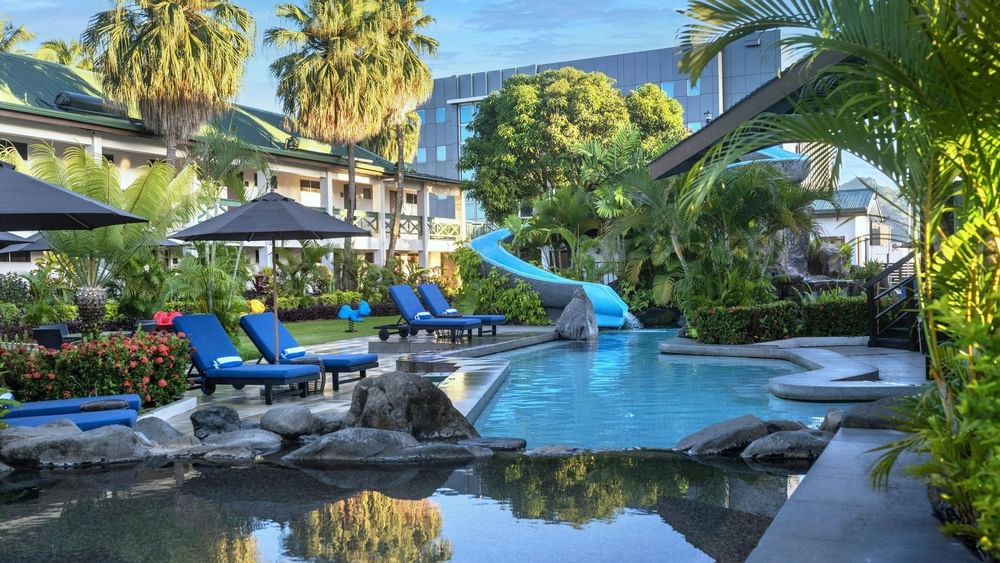 Bright blue loungers under a black patio umbrella by a winding swimming pool at TokaToka Resort Nadi Fiji