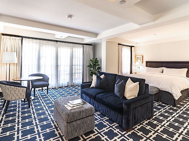 Spacious suite at El Prado Hotel, with a large bed, navy sofa, and ample seating area