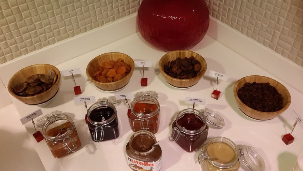 Breakfast & In-Room Dining with Jars of jam by wooden bowls of dried fruit surrounding a red vase at Warwick Ankara