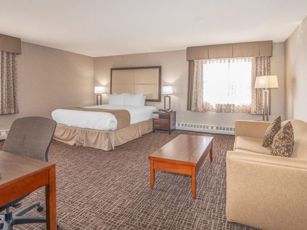 A hotel room with a king bed, couch, desk, chair, coffee table, lamps, and framed picture.