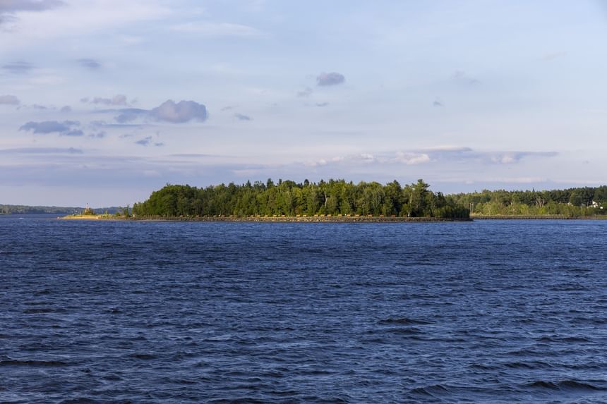 Green forest island in a wide blue river under clouds near Rodd Miramichi River, a top choice hotel in Miramichi, NB