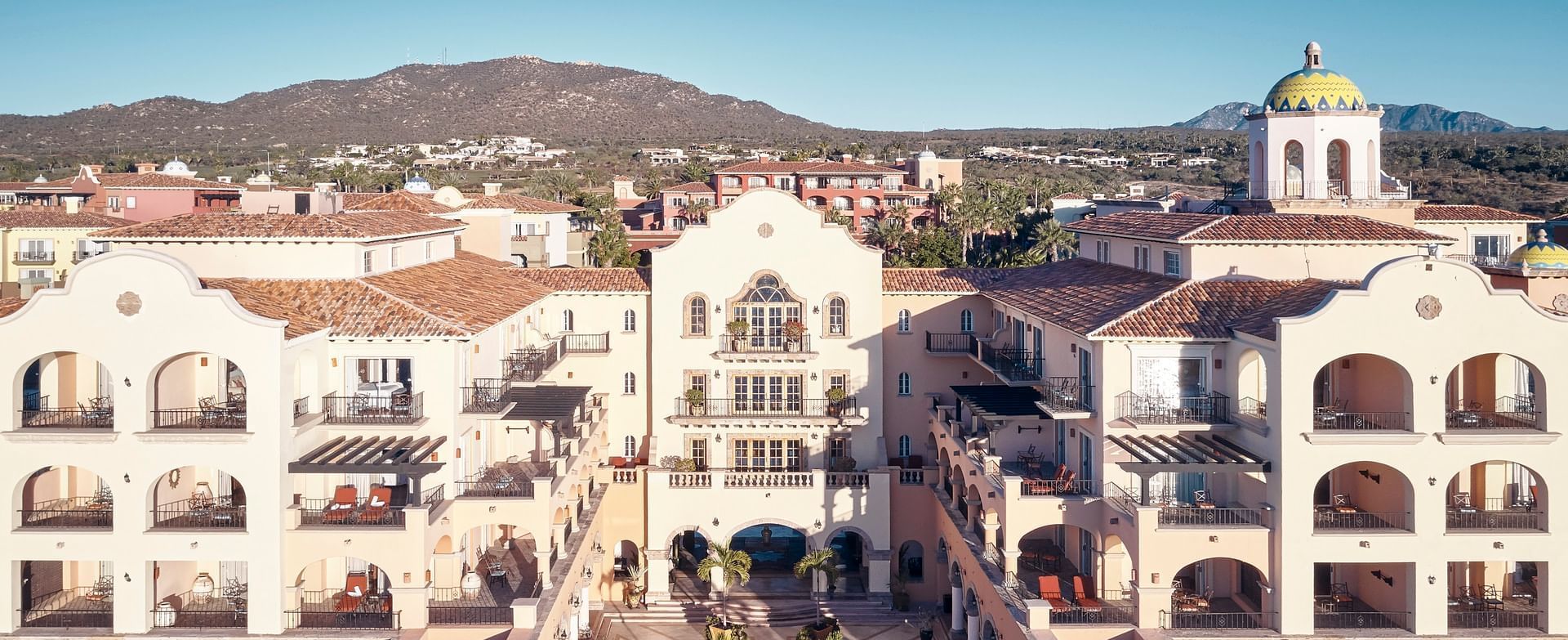 Vista aérea de un resort Hacienda del Mar Los Cabos de estilo colonial, con patios y un fondo montañoso.
