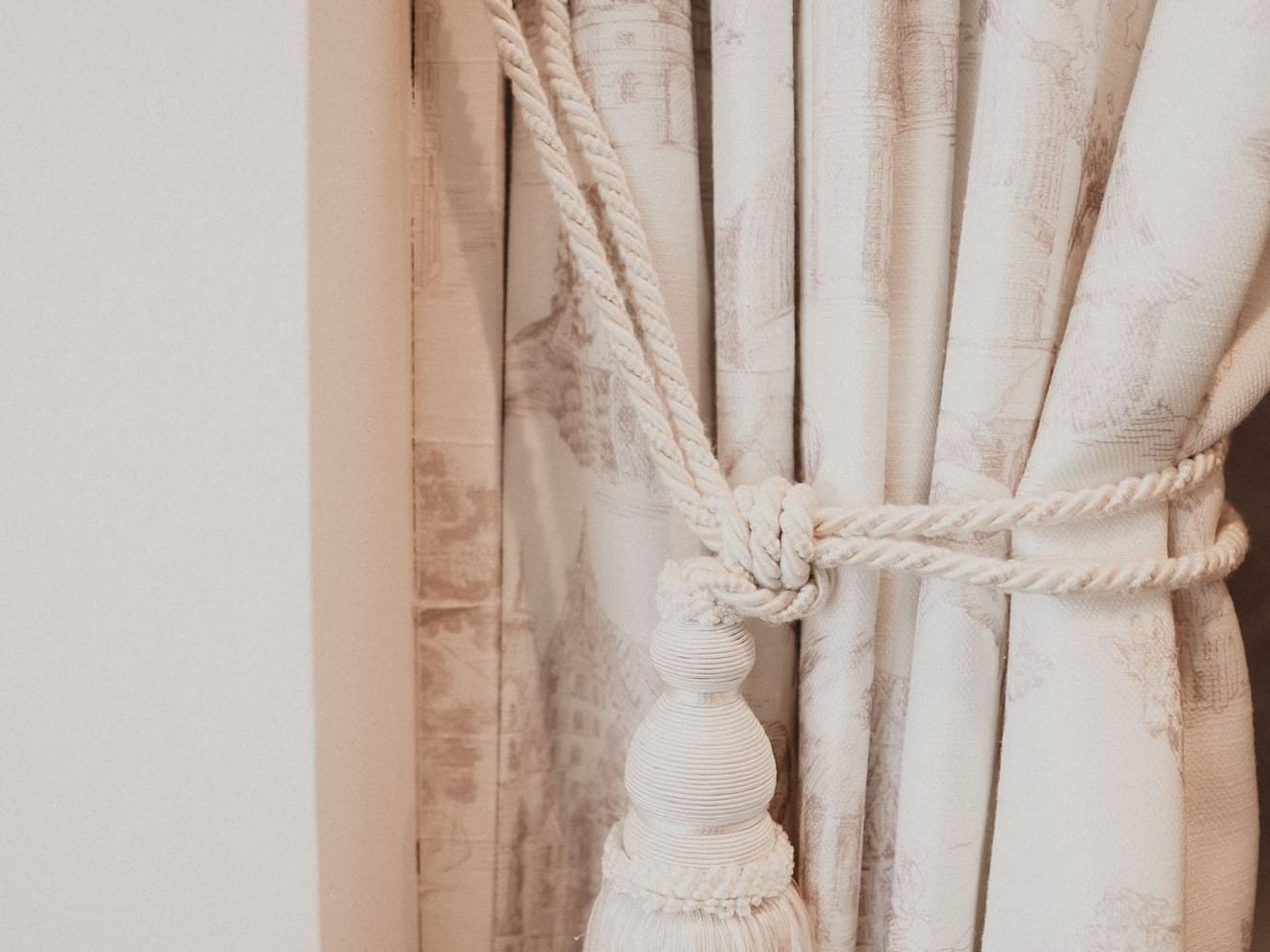 White curtain with a tassel and cord tied in a knot, hanging on a rod.