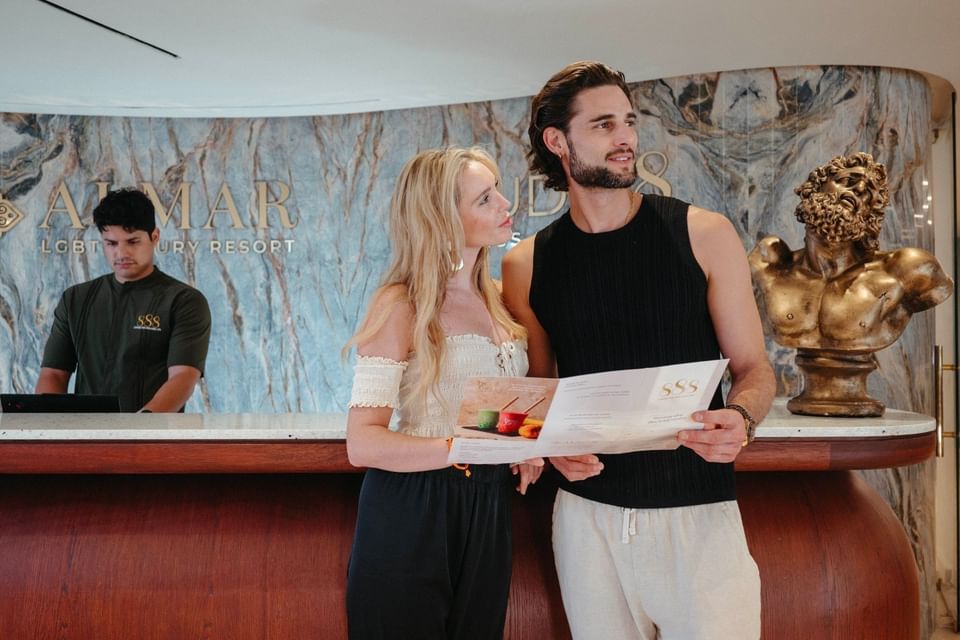 Couple checking in at marble reception desk with staff member and gold sculpture at Almar LGBT Luxury Resort