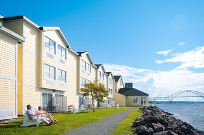 Couple on chairs by a yellow hotel building under a clear blue sky, with a river near Rodd Miramichi River