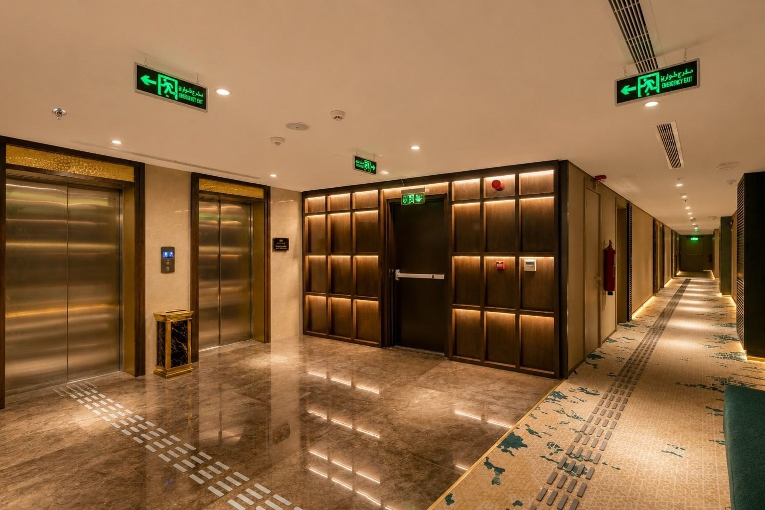 Elevator lobby with shiny tiled floors opening into a long carpeted hallway inside the hotel Naviti by Warwick Jeddah