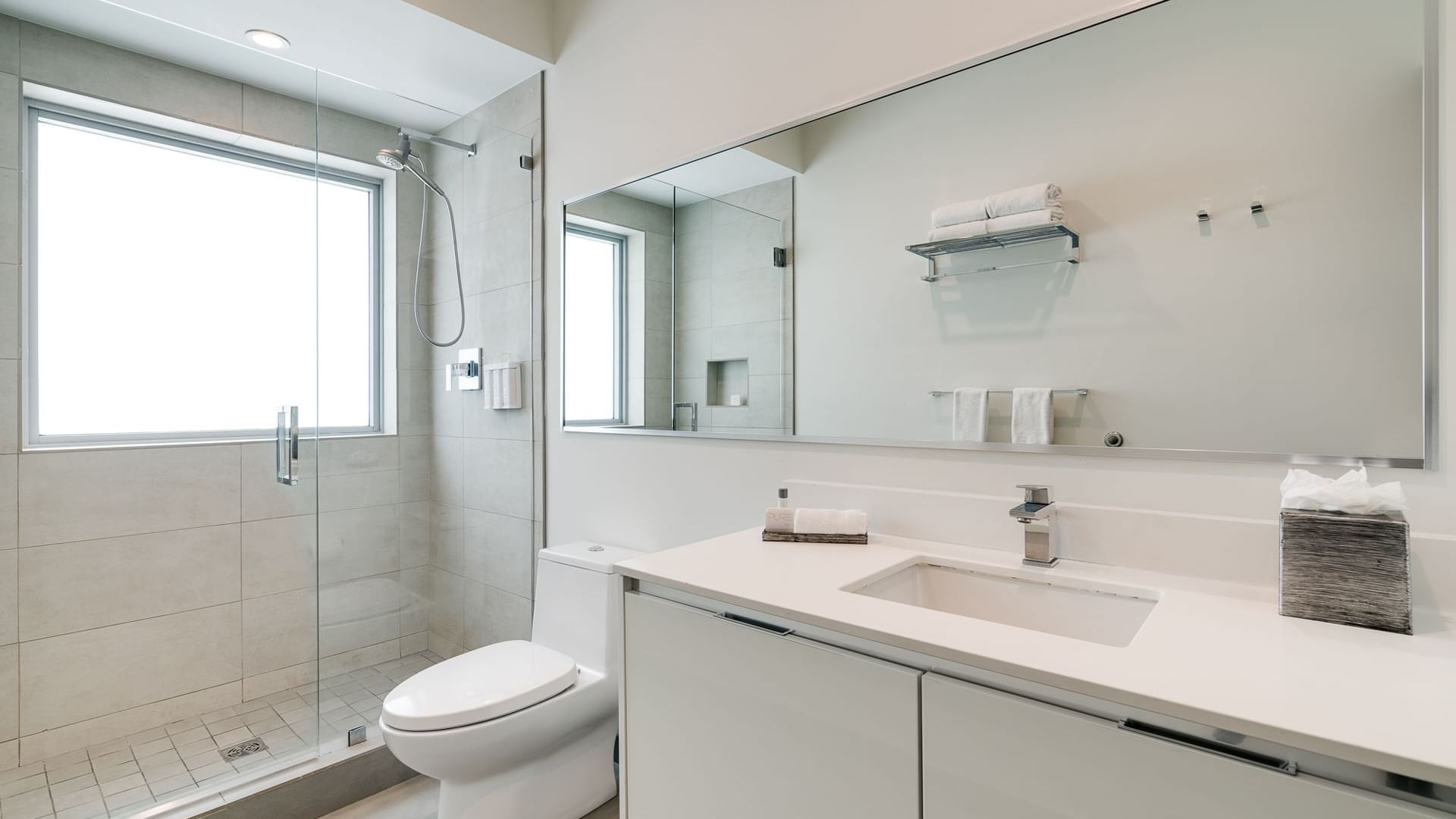 A clean and modern bathroom with a large mirror, white sink, and separate glass-enclosed shower.