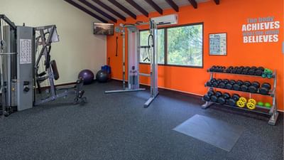 Fitness equipment and dumbbell rack by an orange wall with motivational quote at Sugar Cane Club Hotel & Spa