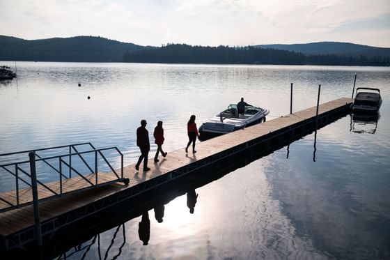 Three people walking on a dock towards a boat on a tranquil lake near The Lodge at Schroon Lake