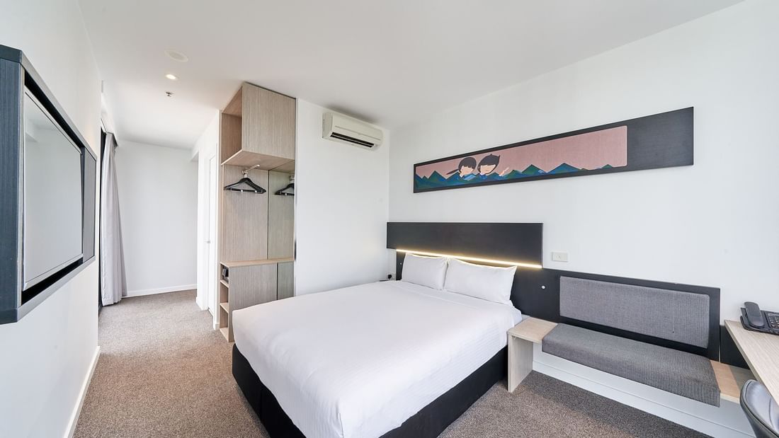 Deluxe Corner Room One Queen Bed featuring a comfortable bed, an open wardrobe, and stylish artwork at Ibis Adelaide