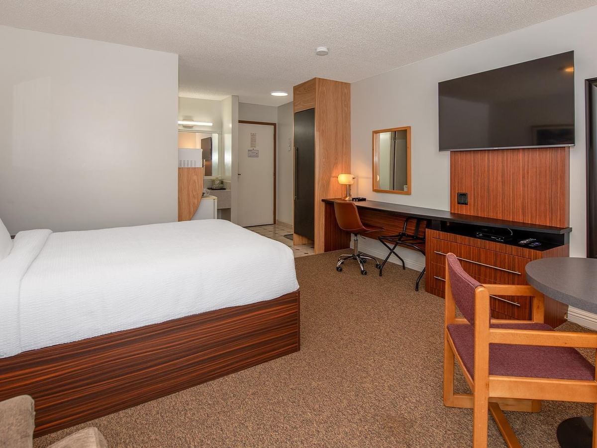 Guest room with a queen bed, work desk, round table and wall-mounted TV