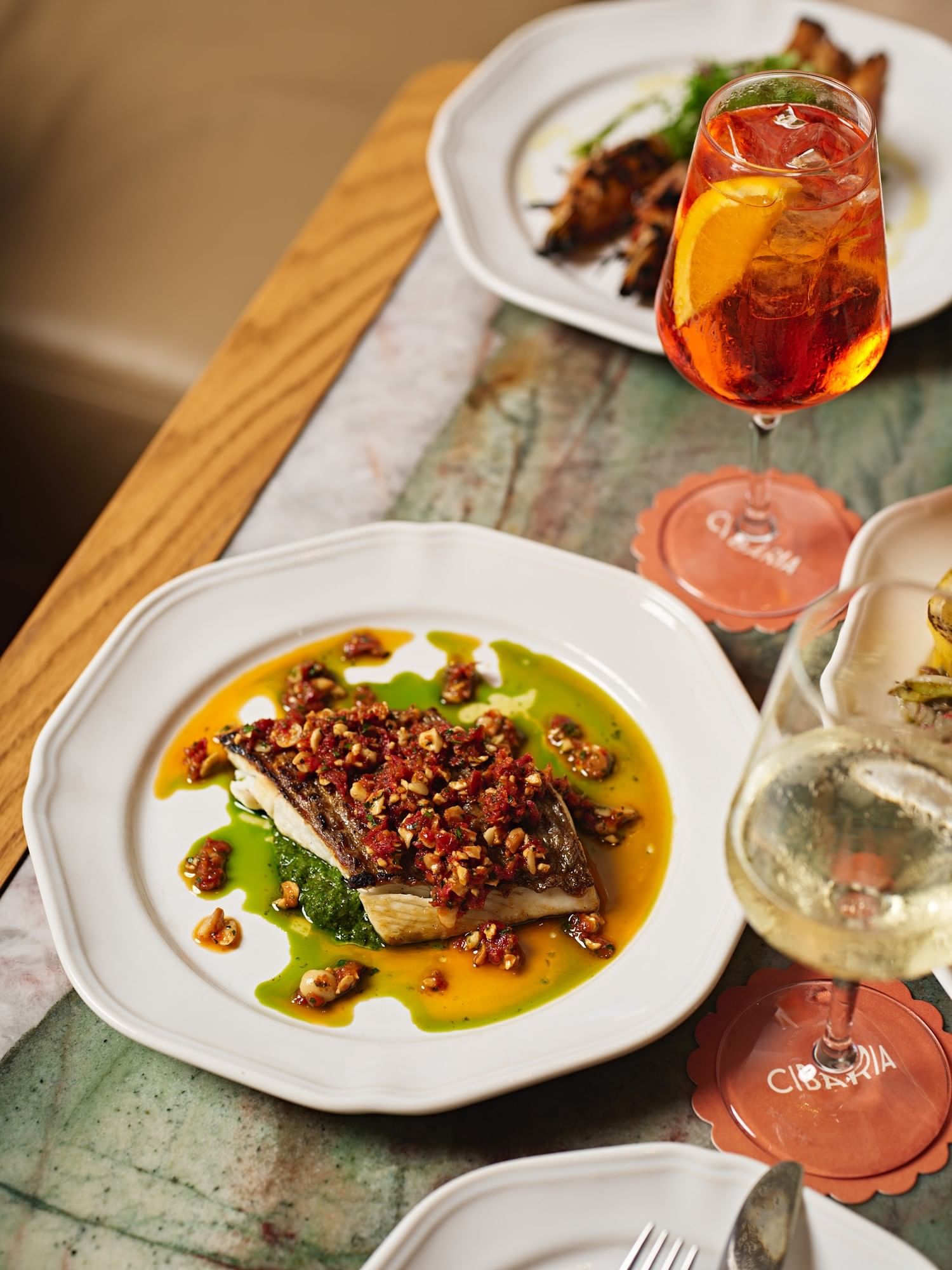 Cibaria at Elysium Hotels serves grilled barramundi on green puree with salsa and an Aperol Spritz on green marble