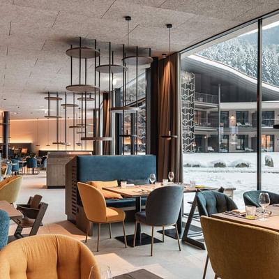 Interno di un ristorante con tavoli e sedie colorate, grandi finestre e vista su un paesaggio innevato.