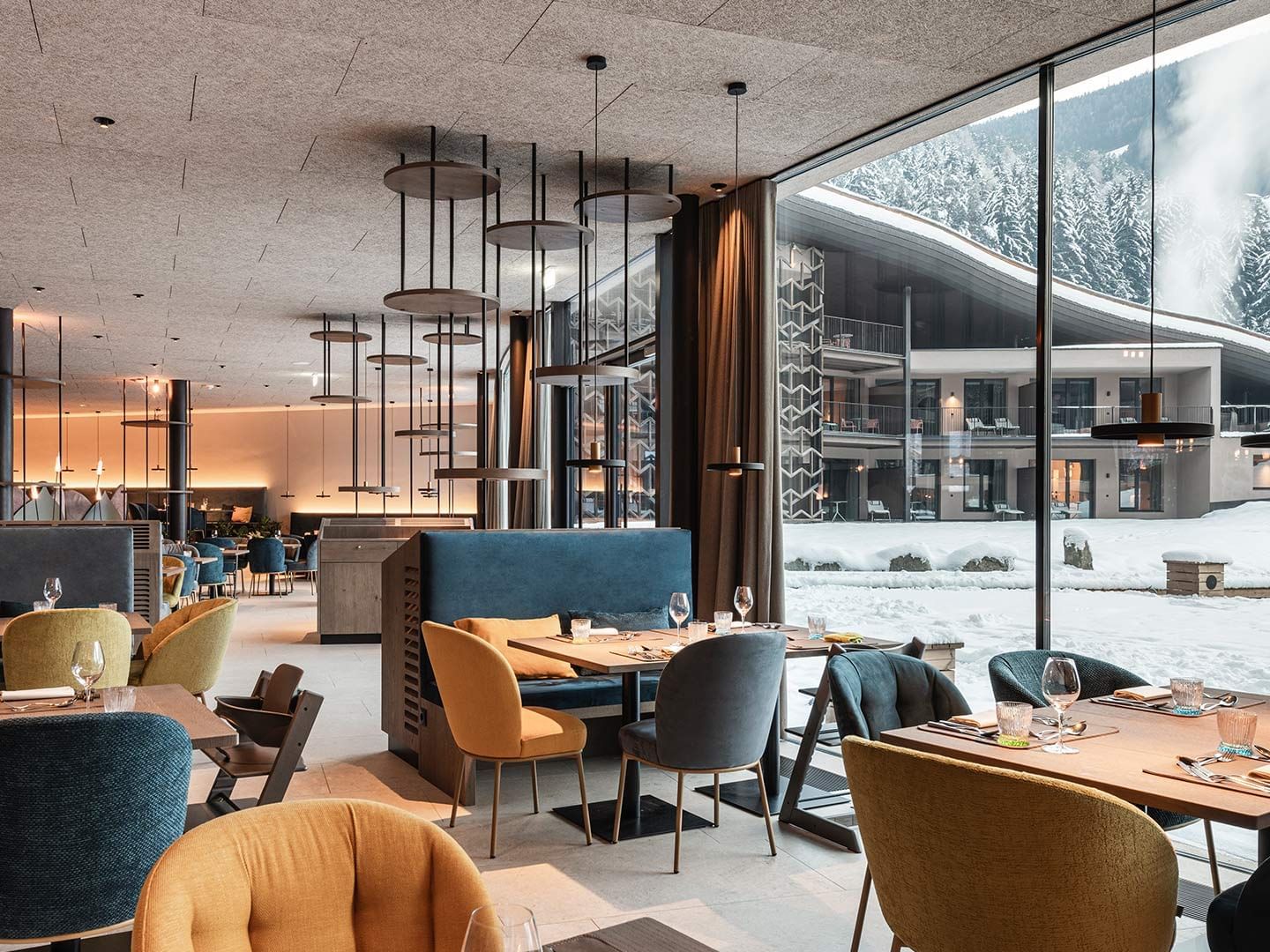 Modernes Restaurant mit bunten Stühlen, großen Fenstern und Blick auf verschneite Berge.