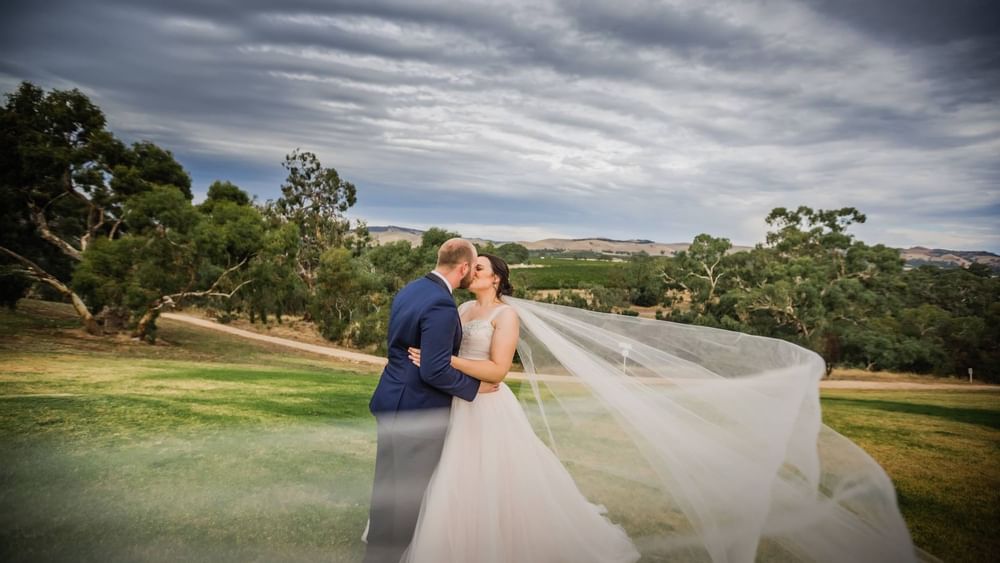 Happy wedding couple kissing & embracing near Novotel Barossa