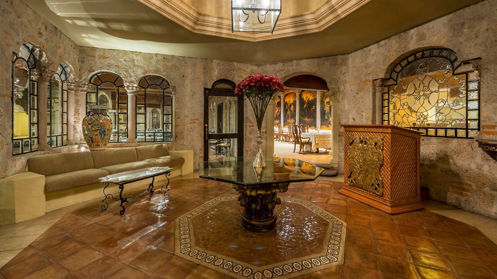 Elegante vestíbulo con paredes de piedra, espejos arqueados y mesa central con flores en Quinta Real Aguascalientes.