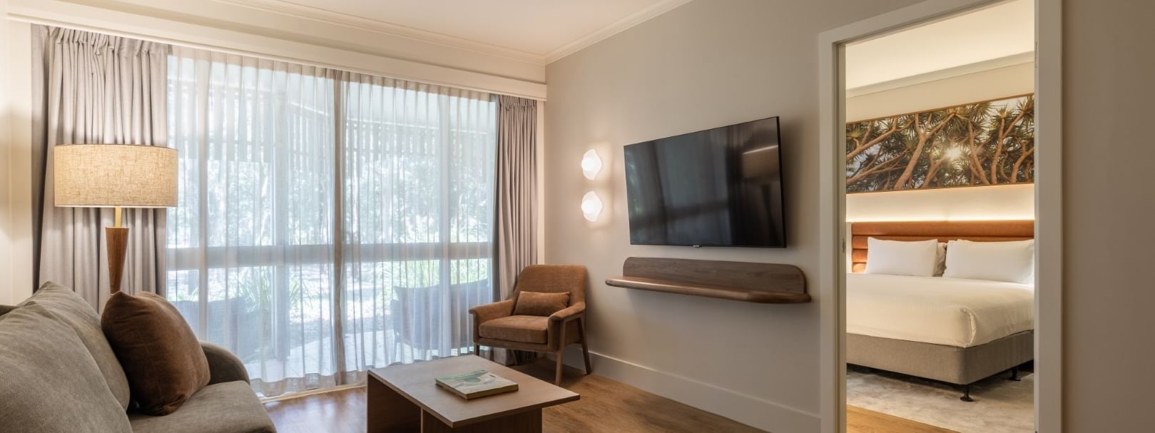Spacious deluxe one bedroom suite with living area, wall-mounted TV, and separate bedroom at Novotel Sunshine Coast.