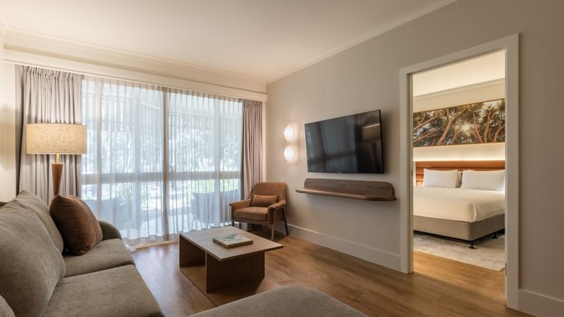 Spacious deluxe one bedroom suite with living area, wall-mounted TV, and separate bedroom at Novotel Sunshine Coast.