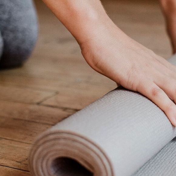 A person unrolling a yoga mat on wooden floor for Presidents’ Week Yoga Sessions.