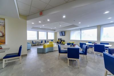 Lounge area with TV & blue chairs and tables arranged at St. Louis Airport Hotel
