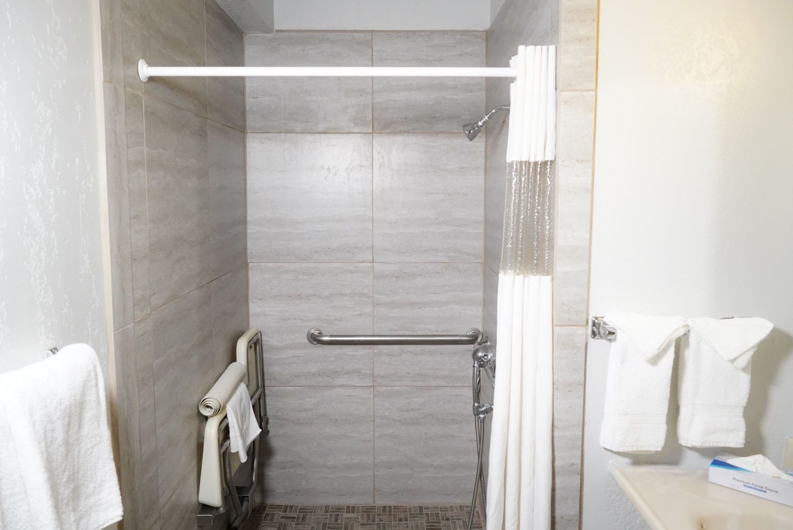 A bathroom shower with gray tiles, a grab bar, and a shower curtain.