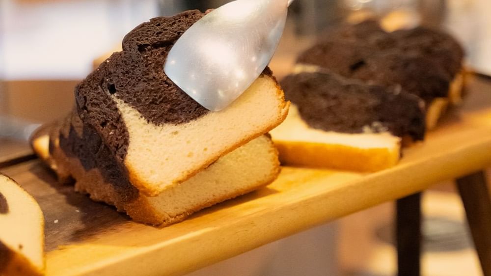 Une tranche de gâteau marbré au chocolat et à la vanille, présentée sur une planche en bois chez Warwick Hotels and Resorts, prête à être servie