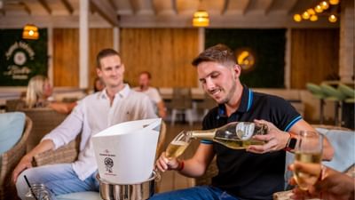 Man pouring sparkling champagne from a chilled bottle into a glass in Sand Street Bistro at Sugar Cane Club Hotel & Spa