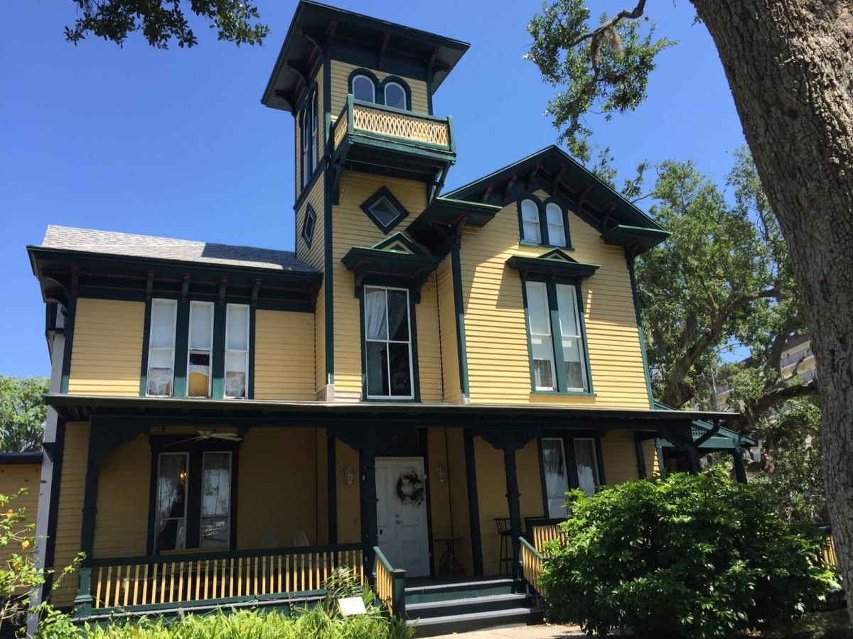 A large yellow house with green trim and a tower