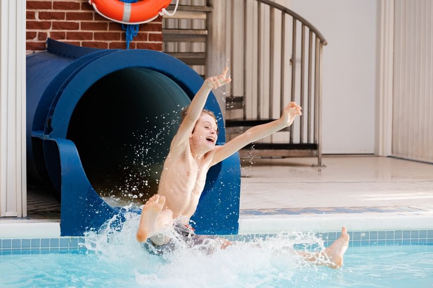 Boy splashing into indoor pool at end of blue slide at Rodd Royalty, among Charlottetown hotels with pools