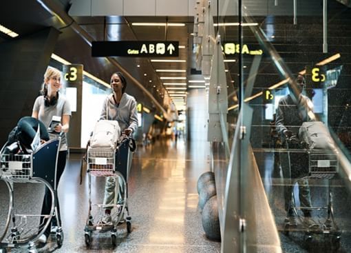 Two travelers with luggage carts inside an airport.