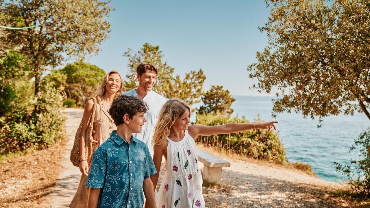 Familie spaziert entlang eines Küstenpfads, während ein Mädchen aufs Meer zeigt.