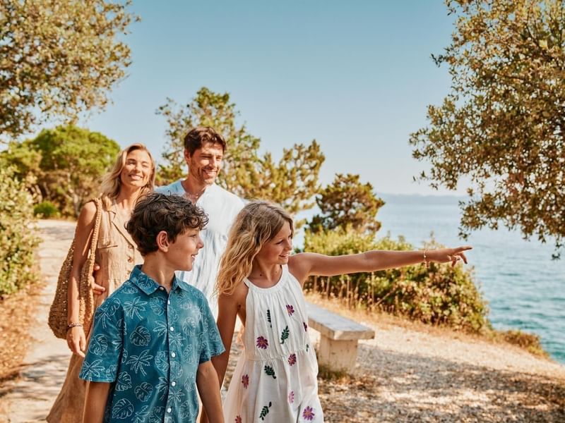 Famiglia cammina lungo un sentiero costiero con una ragazza che indica il mare.