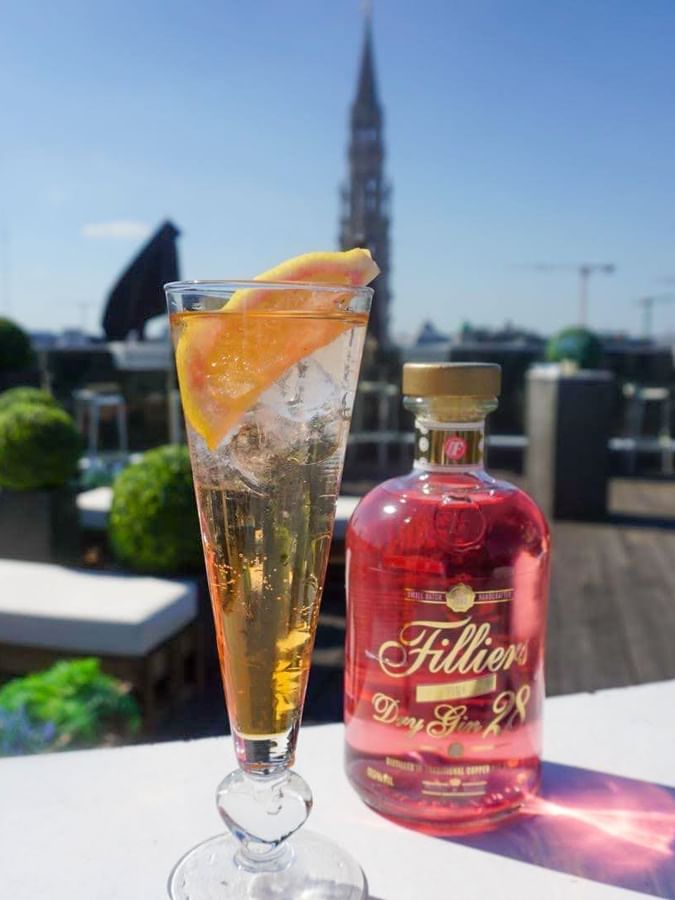 Refreshing gin cocktail with pink gin bottle on a wooden outdoor terrace at Warwick Grand Place Brussels
