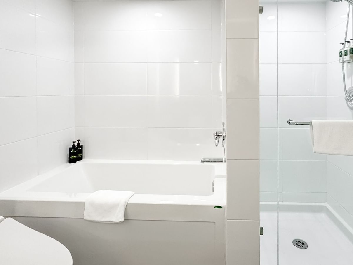 Hotel bathroom with toilet, bathtub, and shower area, all featuring white fixtures and tiles.