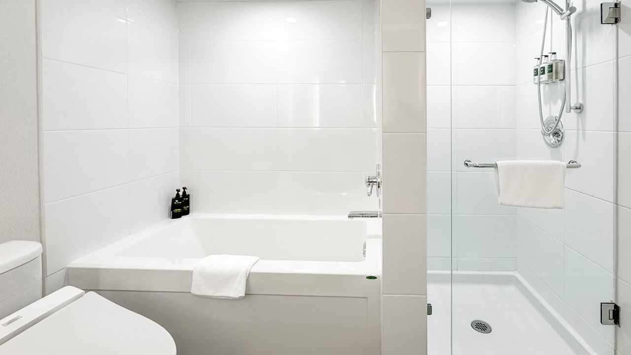 Hotel bathroom with toilet, bathtub, and shower area, all featuring white fixtures and tiles.