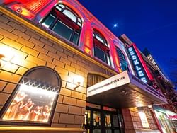Illuminated facade of Berkeley Performance Center at night with a poster of performers in the window.