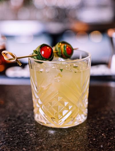 Vaso de cristal con bebida y palillo de aperitivo con tomate cereza y hierba.