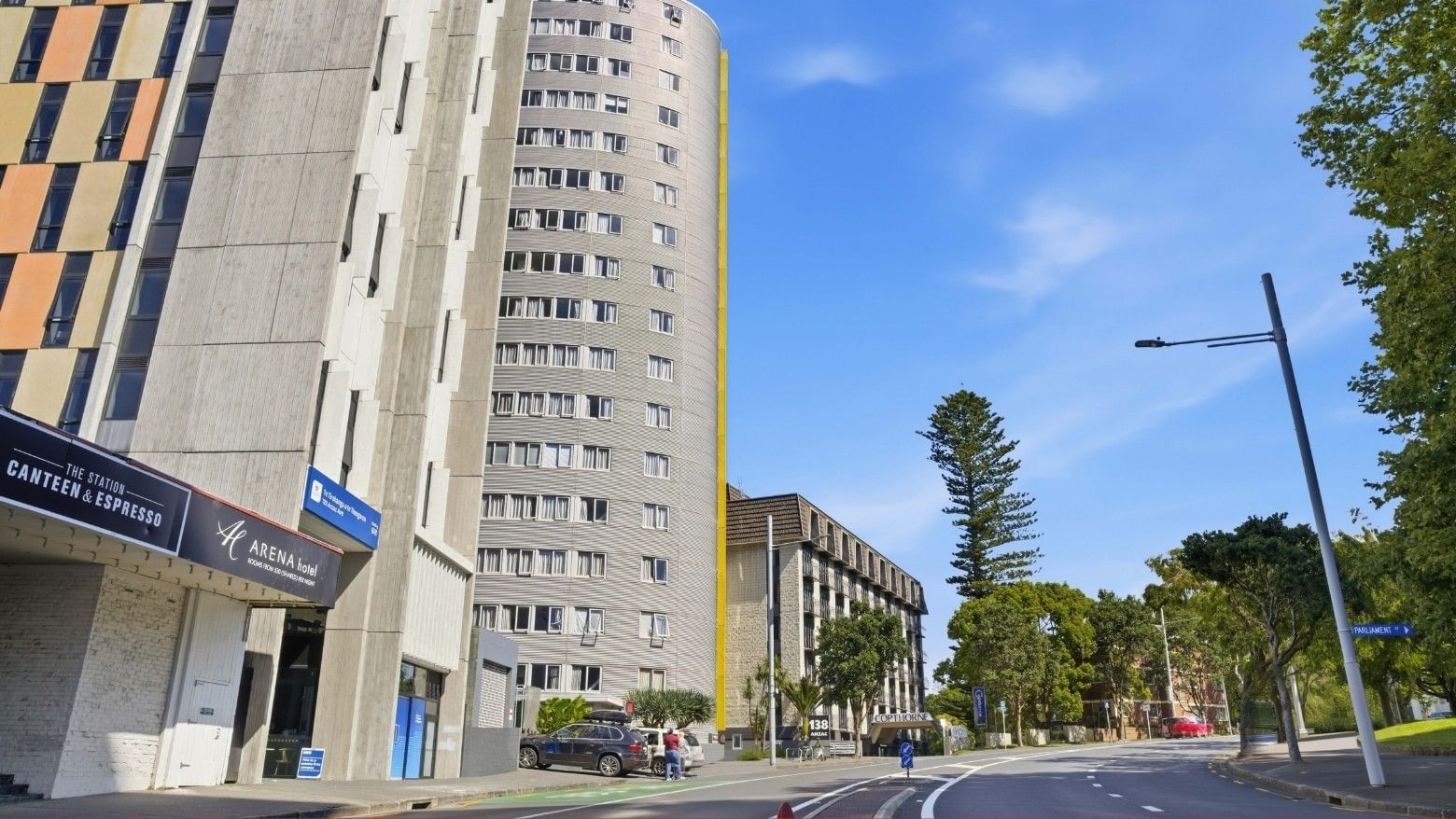 Tall buildings with many windows and cars parked on the street in front of Student Living Auckland Beach.