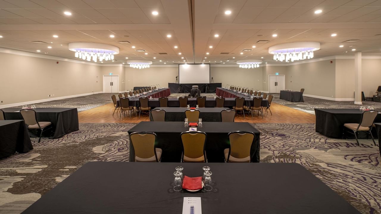 Spacious conference room with tables, chairs, and a projector screen at Coast Nisku Inn & Conference Centre.