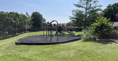Outdoor playground with a swing set and slide on black mulch near an American flag at Branson Hillside Hotel