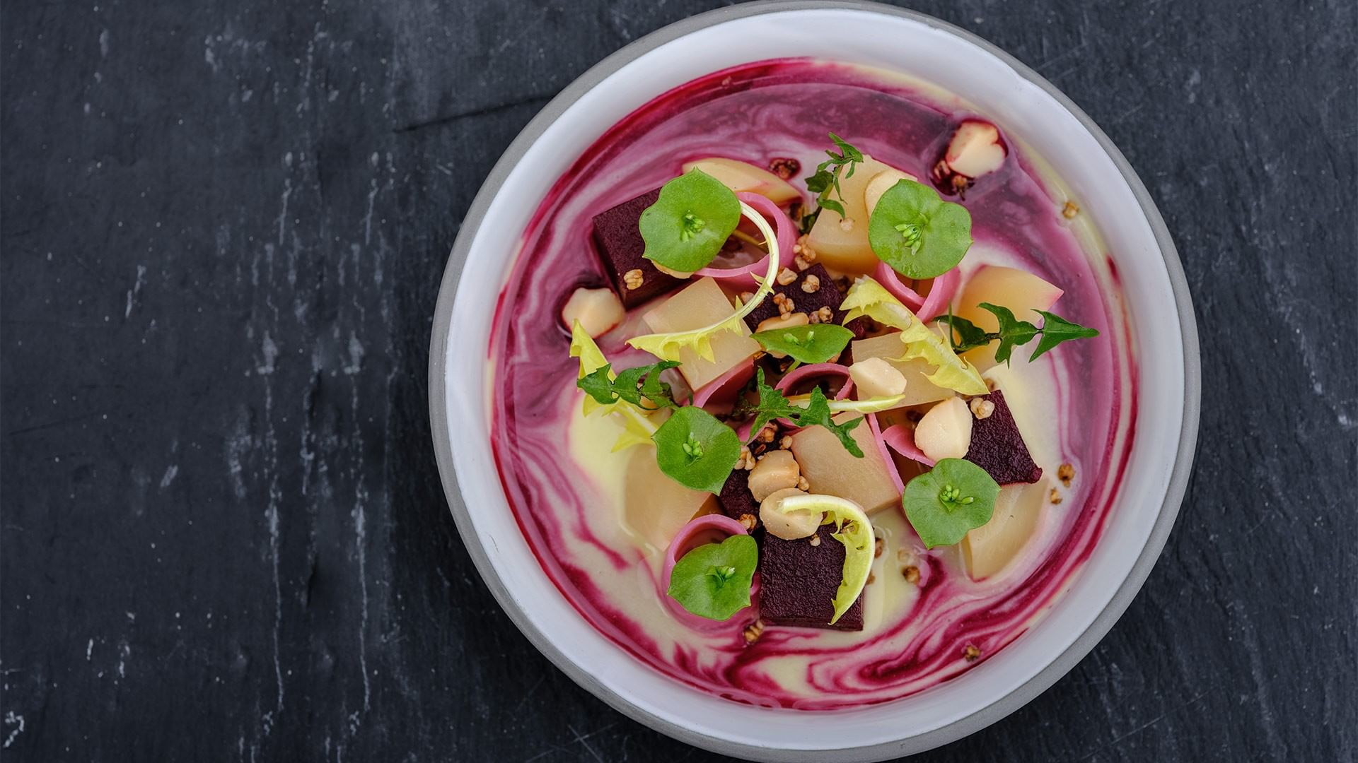 Schüssel mit pinker Suppe, Kartoffeln, Rote Bete und grünen Blattgemüsestücken.