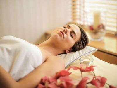 Woman relaxing on a massage table with red petals and a candle in a spa setting.