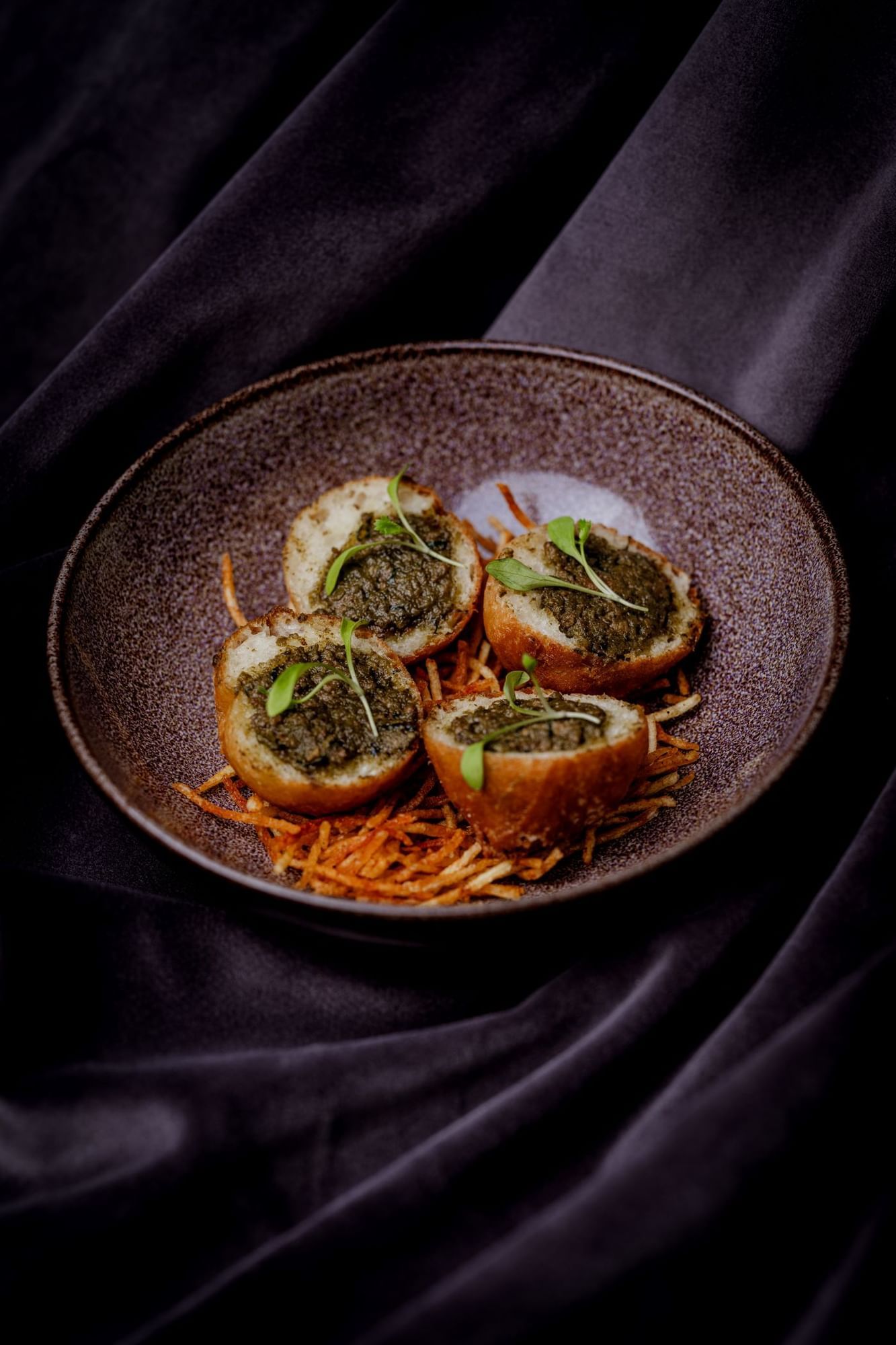 Four stuffed potato rounds on a brown plate with garnishes and shredded carrots at The May Fair Hotel, London.