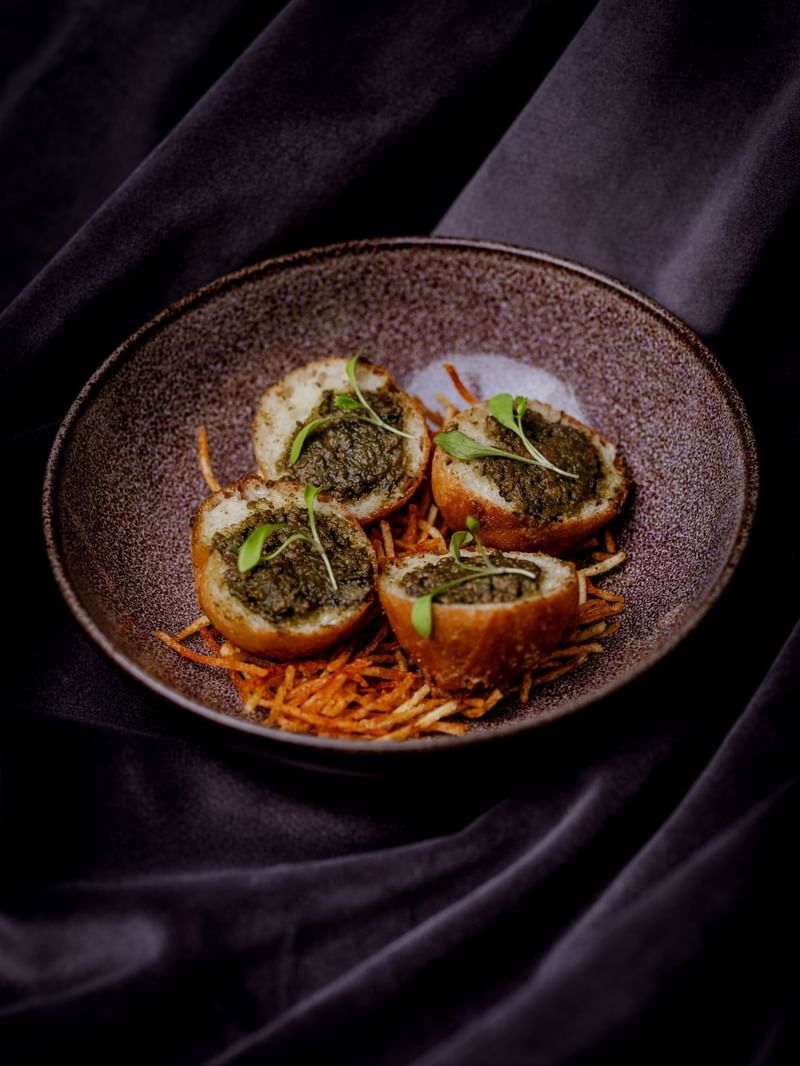 Four stuffed potato rounds on a brown plate with garnishes and shredded carrots at The May Fair Hotel, London.
