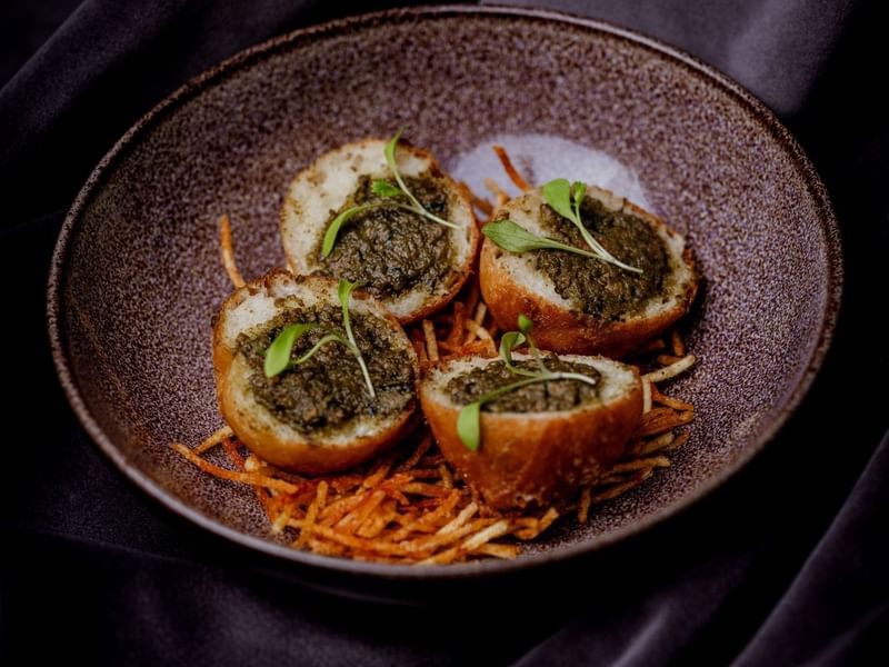 Four stuffed potato rounds on a brown plate with garnishes and shredded carrots at The May Fair Hotel, London.