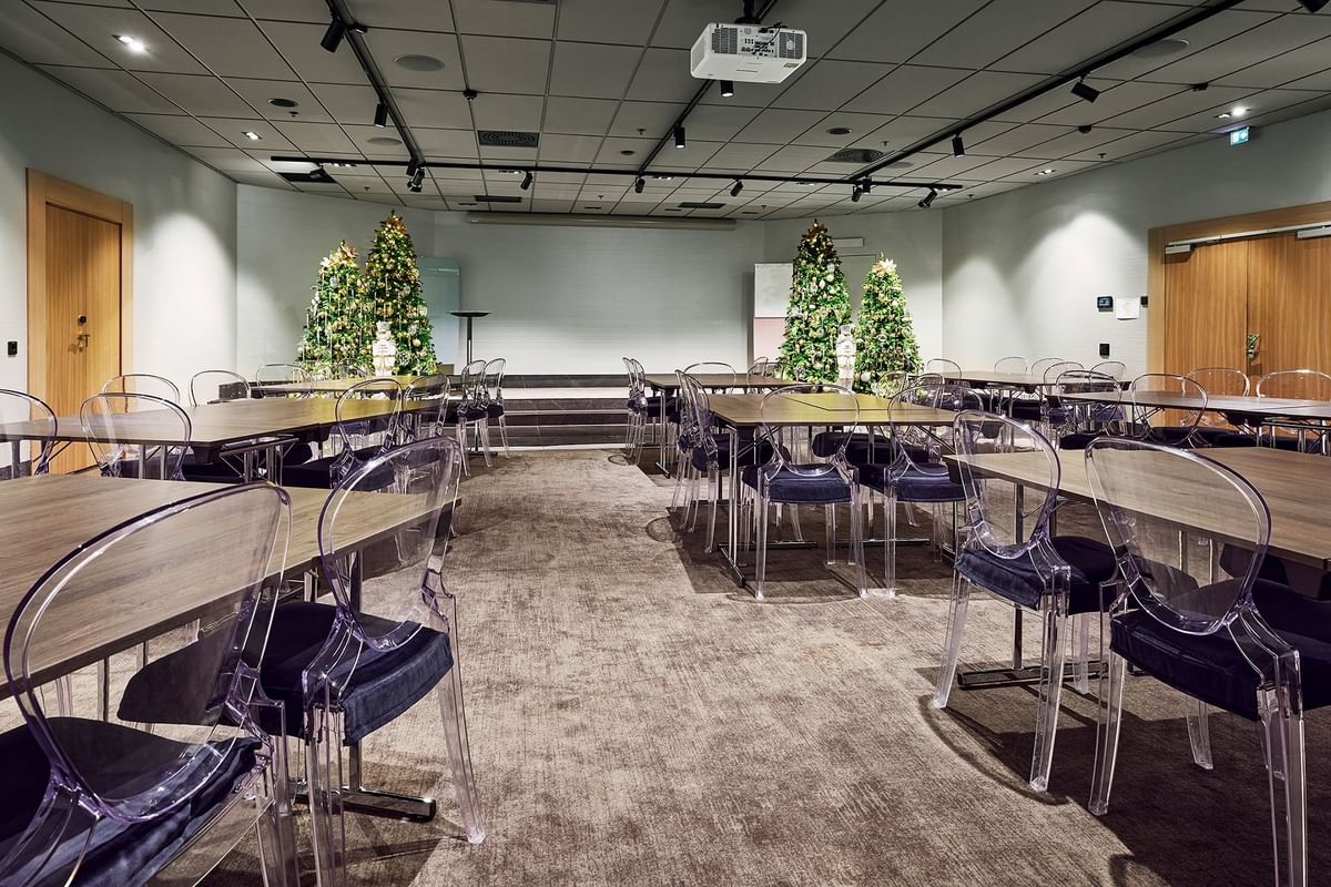 Konferensrum med bord och stolar, dekorerat med julgranar och en projektor på taket.