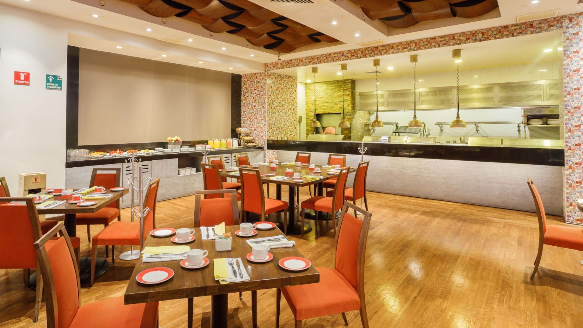 Modern buffet area in Bistro Cafe featuring orange chairs and an open-concept kitchen at Camino Real Pedregal Mexico
